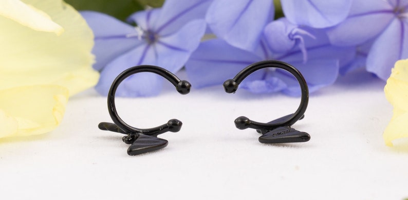 Pu&ograve; includere: Un paio di orecchini a cerchio neri con un design triangolare. Gli orecchini sono aperti e pronti per essere indossati.