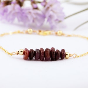May include: A delicate gold chain bracelet with a row of small, dark red gemstone beads.