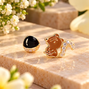 Può includere: Un paio di orecchini a lobo color oro con un design a scoiattolo in smalto marrone e zirconi trasparenti sulla coda, insieme a un orecchino abbinato con una cupola in smalto nero liscio e una base di zirconi trasparenti.
