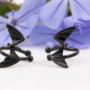 Pu&ograve; includere: Un paio di anelli regolabili a forma di pipistrello nero. Gli anelli sono in metallo e hanno una finitura lucida.