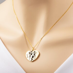 May include: A gold chain necklace with a heart-shaped pendant featuring a black and white photo of a dog. The pendant is engraved with the word "Toby".