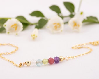 May include: A gold chain bracelet with a row of colorful gemstone beads. The beads are clear, light blue, green, pink, and purple.