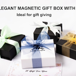 Pu&ograve; includere: Tre scatole regalo con nastri di diversi colori. Le scatole sono nere con interno bianco. I nastri sono verde chiaro, blu e oro. Le scatole sono su una superficie bianca. Il testo "Luzie Crafts" e "A Gift For You" &egrave; stampato sulle scatole.