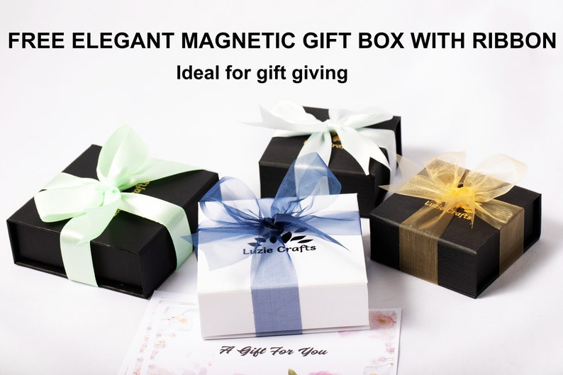 Pu&ograve; includere: Tre scatole regalo con nastri di diversi colori. Le scatole sono nere con interno bianco. I nastri sono verde chiaro, blu e oro. Le scatole sono su una superficie bianca. Il testo "Luzie Crafts" e "A Gift For You" &egrave; stampato sulle scatole.