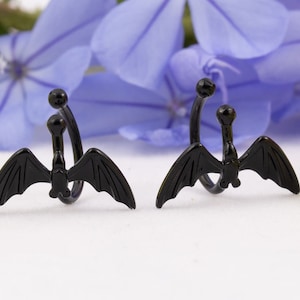 Pu&ograve; includere: Un paio di orecchini a cerchio per orecchie a forma di pipistrello nero. Gli orecchini sono in metallo e hanno un design a spirale. Le ali di pipistrello sono dettagliate e hanno una finitura nera.