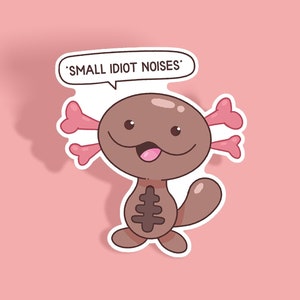 Op de afbeelding: Een sticker met een cartoon axolotl met een bruin lichaam, roze kieuwen en een tekstballon met de tekst 'SMALL IDIOT NOISES'. De axolotl heeft een vrolijke uitdrukking met zijn tong uit, tegen een roze achtergrond.