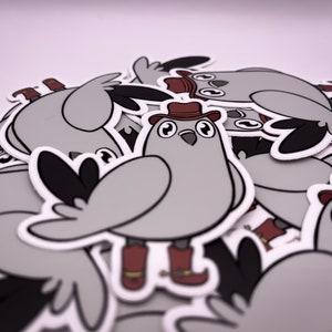 Op de afbeelding: Een stapel grijze en witte vogel stickers met rode cowboyhoeden en laarzen. De stickers zijn cartoonachtige illustraties van vogels die cowboyhoeden en laarzen dragen.
