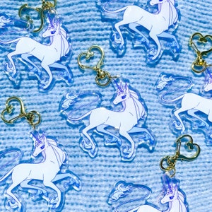 May include: A set of seven clear acrylic keychains featuring a white unicorn with a blue mane and tail. Each keychain has a gold metal ring and a heart-shaped clasp.