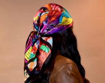 May include: A woman with long black hair is wearing a brown leather jacket and a colorful silk scarf tied around her head.