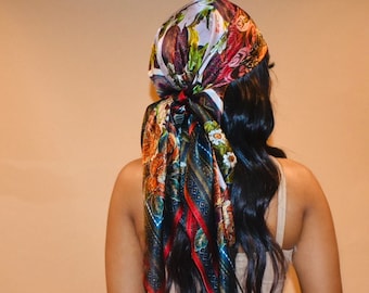 May include: A colorful silk scarf with a floral and paisley design. The scarf features a mix of red, orange, blue, and green hues. The scarf is tied at the back of the head, with long, dark hair cascading down.