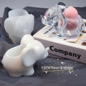 Puede incluir: Tres moldes de silicona en forma de elefante blanco. Los moldes est&aacute;n dise&ntilde;ados para crear artesan&iacute;as de resina. Los moldes se muestran sobre una superficie gris con un libro titulado "The White Company" en el fondo.