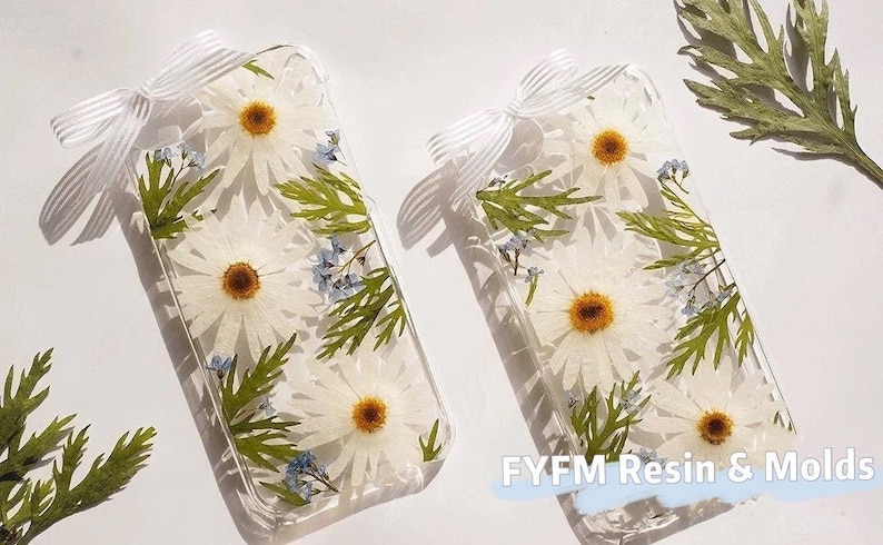 May include: Two clear phone cases with white daisies and green leaves pressed inside. The cases have white bows on the top. The text "FYFM Resin & Molds" is visible at the bottom of the image.