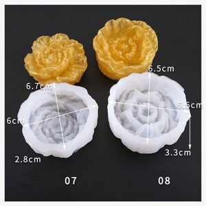 May include: Two flower-shaped molds, one gold and two white, with measurements. The gold flower is solid, while the white ones are molds. One white mold is 6 cm by 6.7 cm, and the other is 6.5 cm by 6.5 cm. The molds are for crafting.