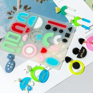 May include: A silicone mold for making earrings with various shapes, including circles, semicircles, arches, and rectangles. The mold is clear and has a variety of colors, including red, green, blue, and pink. There are several finished earrings made with the mold, including a pair with the text "for me" and a pair with the text "one yet".