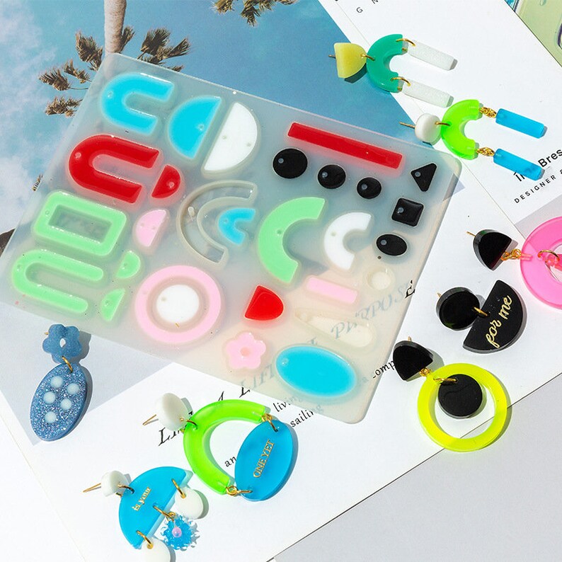 May include: A silicone mold for making earrings with various shapes, including circles, semicircles, arches, and rectangles. The mold is clear and has a variety of colors, including red, green, blue, and pink. There are several finished earrings made with the mold, including a pair with the text "for me" and a pair with the text "one yet".