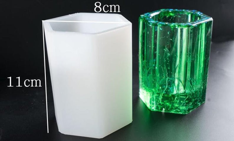 May include: A white, hexagonal-shaped silicone mold, 11 cm tall and 8 cm wide, next to a green, hexagonal-shaped resin casting. The resin casting has a textured surface and is filled with bubbles.