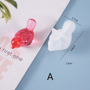 May include: A clear silicone mold shaped like a bird with a 4.6 cm length, 2.7 cm height, and 1.6 cm width. The mold is shown next to a pink bird figurine.