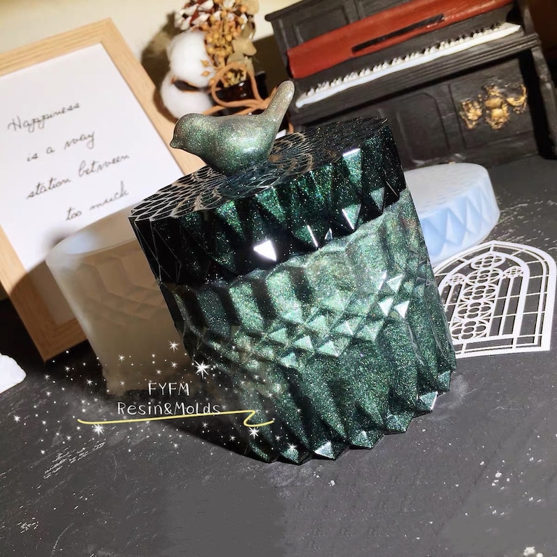 May include: A faceted, dark green resin box with a bird-shaped lid. The box has a geometric design and a glittery finish. The text "FYFM Resin & Molds" is visible on the bottom. A framed quote is in the background.