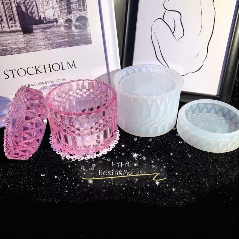 May include: A pink, faceted resin container with a matching lid, sitting on a white lace doily. Next to it are two other resin molds, one white and one clear, with geometric patterns. The image includes the text "FYFM Resin & Molds."