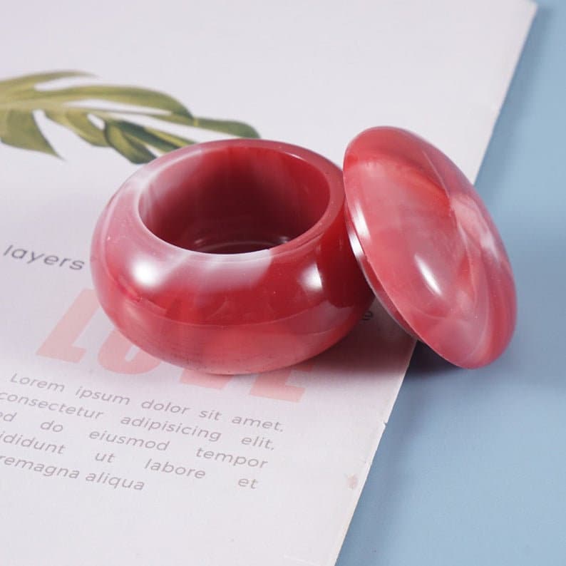 May include: A small, red and white marbled trinket box with a lid. The box is round and has a smooth, glossy finish.
