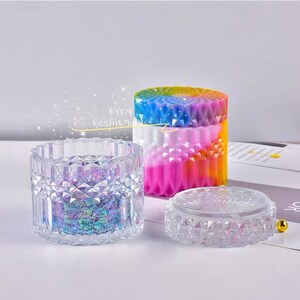 May include: Three decorative containers. One is clear with a geometric pattern and filled with iridescent glitter. Another is a cylindrical container with a rainbow-colored lid and body. A third, smaller container with a lid is also clear.