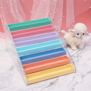 Pode incluir: Um suporte de exibi&ccedil;&atilde;o em camadas de acr&iacute;lico transparente com prateleiras coloridas do arco-&iacute;ris. O suporte est&aacute; vazio e pronto para ser preenchido com itens.
