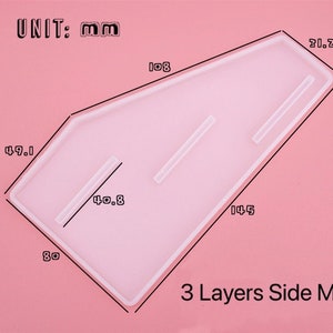 Pode incluir: Um molde de silicone transparente para criar pe&ccedil;as laterais de tr&ecirc;s camadas. O molde tem a forma de um trap&eacute;zio com cantos arredondados e mede 14,5 cm por 8 cm por 4,9 cm. O molde tem tr&ecirc;s canais para criar camadas. UNIT: mm