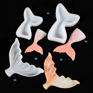 Puede incluir: Una variedad de moldes y colas de sirena terminadas en varios colores. Los moldes son blancos, y las colas terminadas son rosas, melocot&oacute;n e iridiscentes. Las colas tienen un aspecto texturizado y escamado. Peque&ntilde;as cuentas azules y verdes est&aacute;n esparcidas sobre un fondo negro.