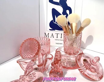 Può includere: Un set di contenitori in vetro rosa con disegni intricati, tra cui un piatto a forma di farfalla, una piccola statuetta e un barattolo con coperchio. I contenitori sono perfetti per riporre piccoli oggetti come gioielli, pennelli per il trucco o altri oggetti da collezione.