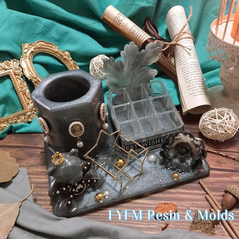 May include: A decorative resin tray with a hexagonal pen holder, a small organizer, and a gold wire rack. The tray features a gray and silver color scheme with pearl accents and a small bear figurine. The text "BEST WISHES" is visible.