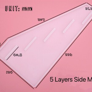 Pode incluir: Um molde de pl&aacute;stico branco para fazer bolos de 5 camadas. O molde tem a forma de um tri&acirc;ngulo com cantos arredondados e tem medidas em mil&iacute;metros marcadas nele. O texto "UNIT: mm" e "5 Layers Side Mold" est&aacute; impresso no molde.