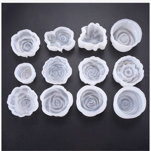 May include: A selection of white silicone rose-shaped moulds. The moulds vary in size and design, with detailed petal patterns. Ideal for crafting, these moulds offer a versatile option for creating decorative elements.