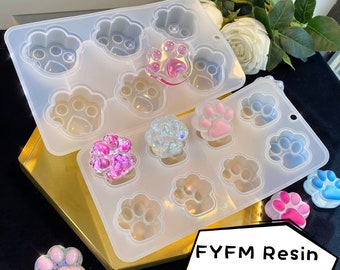 May include: Two silicone molds for making paw print resin crafts. The molds are clear and have a paw print design. There are several finished paw print resin pieces in various colors, including pink, blue, and iridescent.