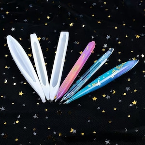 May include: An assortment of pens and molds. Three white, elongated molds are arranged with three pens. The pens are pink, blue, and clear with glitter and the words "a wish with than" on the blue pen.