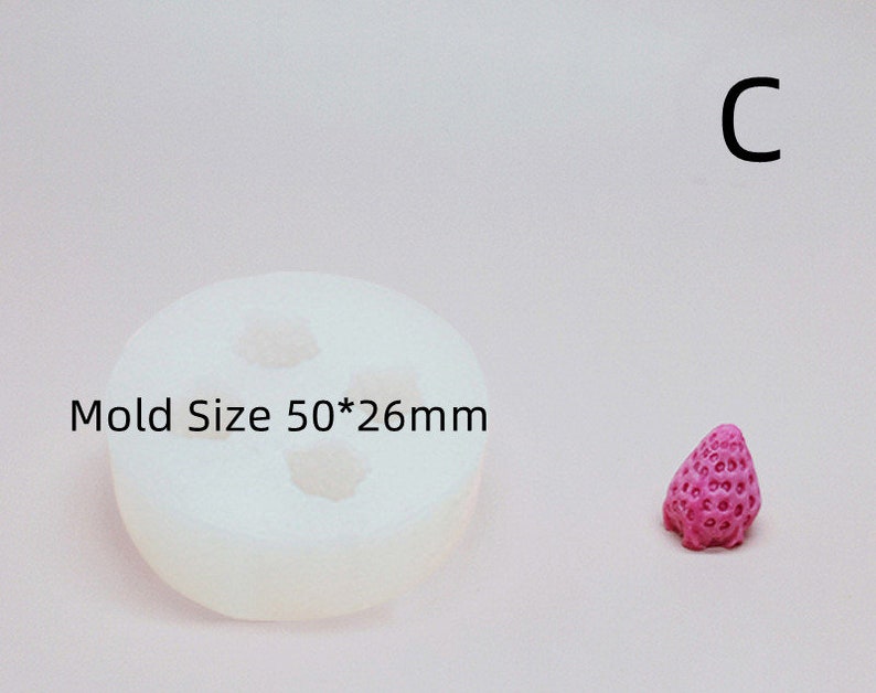 Op de afbeelding: Een witte siliconen mal voor het maken van snoepjes in de vorm van een aardbei. De mal is 50 mm bij 26 mm en wordt getoond naast een roze aardbei-vormig snoepje.