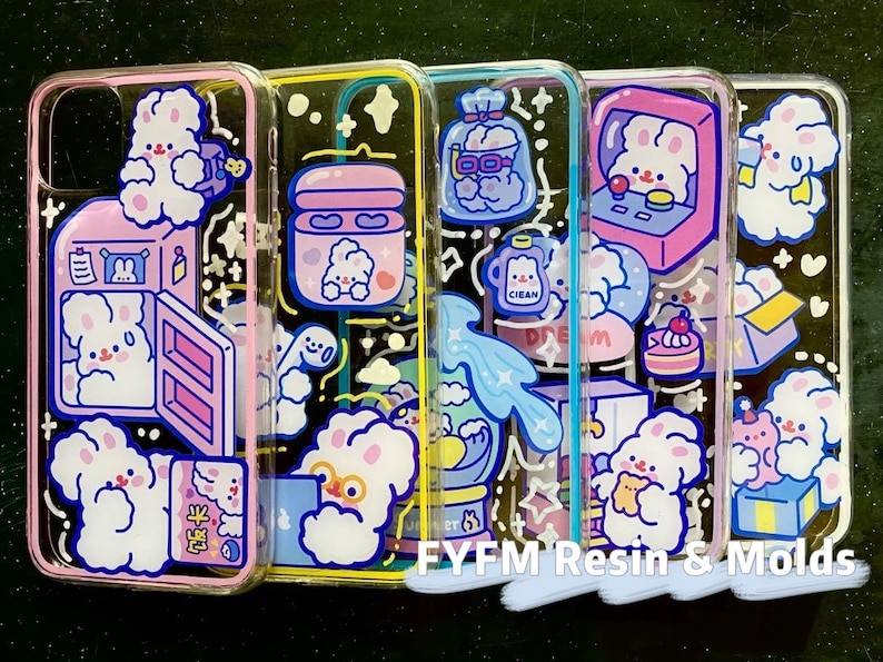 May include: Four clear phone cases with colorful cartoon designs. Each case features a different design with a cute bunny, a cloud, a bottle of soap, and a kitchen appliance. The cases are all made of clear plastic and have a glossy finish.