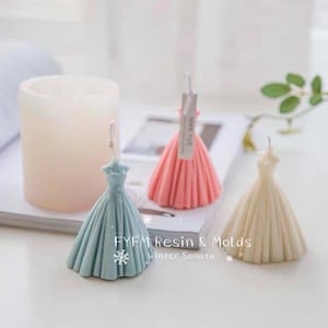 May include: Three decorative candles shaped like wedding dresses. The candles are in blue, pink, and white.