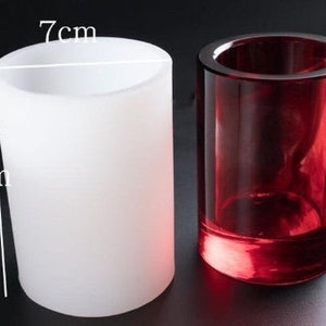 May include: Two cylindrical candle holders. One is frosted white, 8.8 cm tall and 7 cm wide. The other is a transparent, deep red. Both are made of glass and are suitable for home decor.
