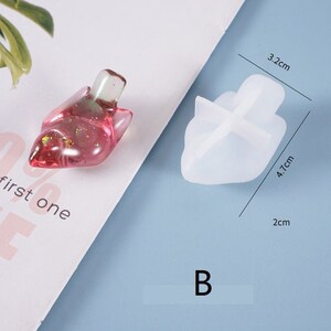 May include: A clear, pink resin object with gold flecks next to a white silicone mold. The resin object is shaped like a shoe. The mold measures 4.7 cm high, 3.2 cm wide, and 2 cm thick. The word "first one" is visible.