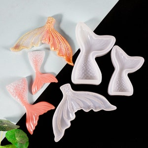 Puede incluir: Una colecci&oacute;n de moldes y piezas de resina terminadas con forma de cola de sirena en tonos rosa, melocot&oacute;n y transparente. Los moldes son de silicona flexible y las piezas terminadas tienen un efecto nacarado brillante. Las colas var&iacute;an en tama&ntilde;o y dise&ntilde;o.