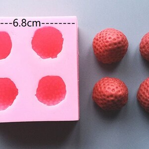 Op de afbeelding: Roze siliconen mal met vier ronde holtes, elk met een diameter van 6,8 cm. Naast de mal zijn vier rode, aardbei-vormige snoepjes te zien.