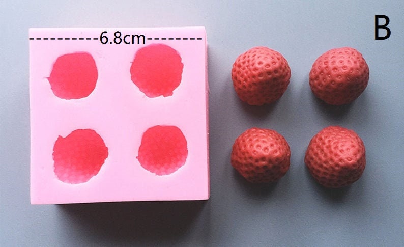 Op de afbeelding: Roze siliconen mal met vier ronde holtes, elk met een diameter van 6,8 cm. Naast de mal zijn vier rode, aardbei-vormige snoepjes te zien.