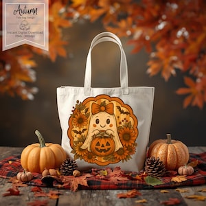 May include: A cream-colored tote bag with a Halloween-themed design. The design features a cartoon ghost holding a jack-o'-lantern, surrounded by sunflowers and bats. The bag is placed on a plaid surface with pumpkins and fall leaves. The text "Autumn Tote Bag Design" is in the upper left corner.