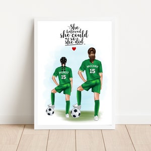 Könnte beinhalten: Zwei weibliche Fußballspielerinnen in grünen Trikots mit den Namen "HURST" und "MCCABE" und der Nummer "15" auf dem Rücken. Der Text "She believed she could so she did." befindet sich oben im Bild mit einem roten Herzen.
