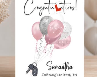 May include: A white greeting card featuring the text Congratulations! with a red L symbol, a cluster of pink and silver balloons, and a car key fob. Below, the name Samantha is printed with the text On Passing Your Driving Test and 27/09/2024.