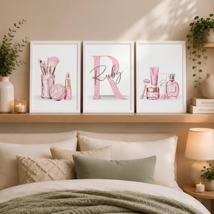 Könnte beinhalten: Drei gerahmte Wandbilder mit rosa Kosmetikmotiven. Das linke Bild zeigt Make-up-Pinsel, einen Puder und Lippenstift. In der Mitte ist ein großer Buchstabe R mit dem Namen Ruby zu sehen. Rechts sind verschiedene Hautpflegeprodukte abgebildet.