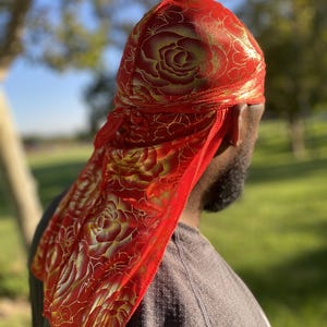May include: A red satin durag with a gold floral pattern. The durag is tied on a person's head.