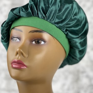 May include: A green satin bonnet with a green elastic band. The bonnet is worn on a mannequin head.