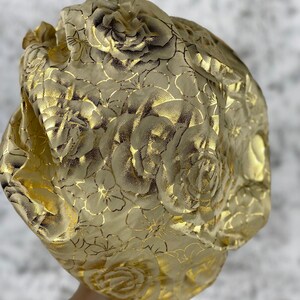 May include: Gold satin sleep cap with a rose pattern. The cap is gathered at the top and has a smooth, silky texture.