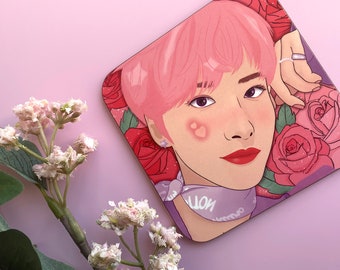 May include: A pink and purple illustrated coaster featuring a person with pink hair and a purple bandana. The person has a heart-shaped blush on their cheek. The background features pink and red roses.